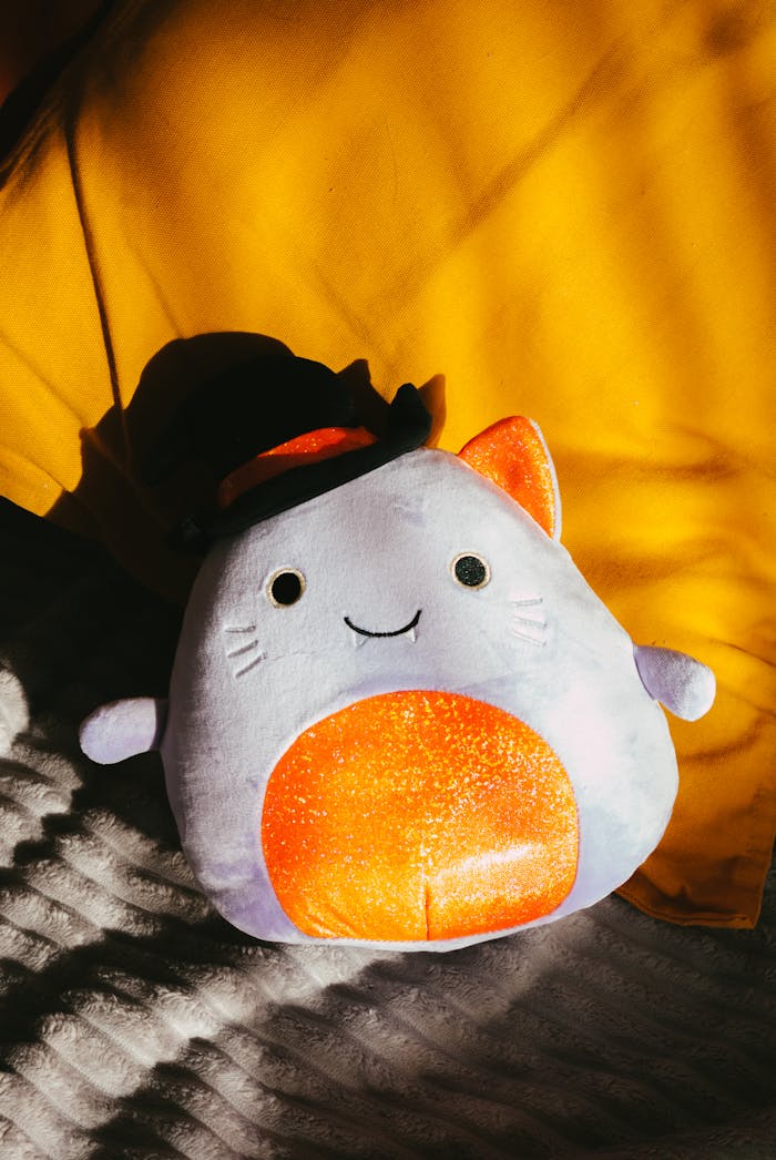 Cute plush cat toy sunlit on yellow and white bedding. Perfect for cozy or playful home decor.